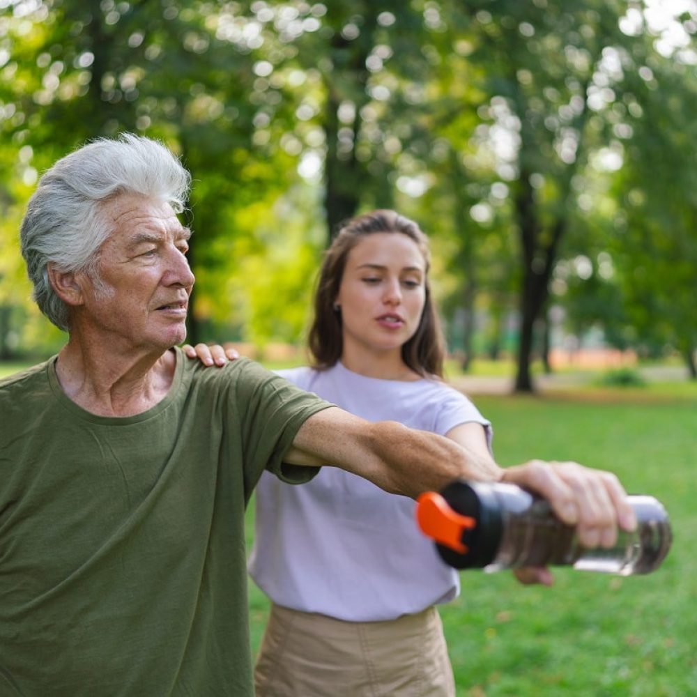 Home Care Services - Transfer Assistance, Exercise, and Mobility. Elderly man with younger woman in park doing exercise.